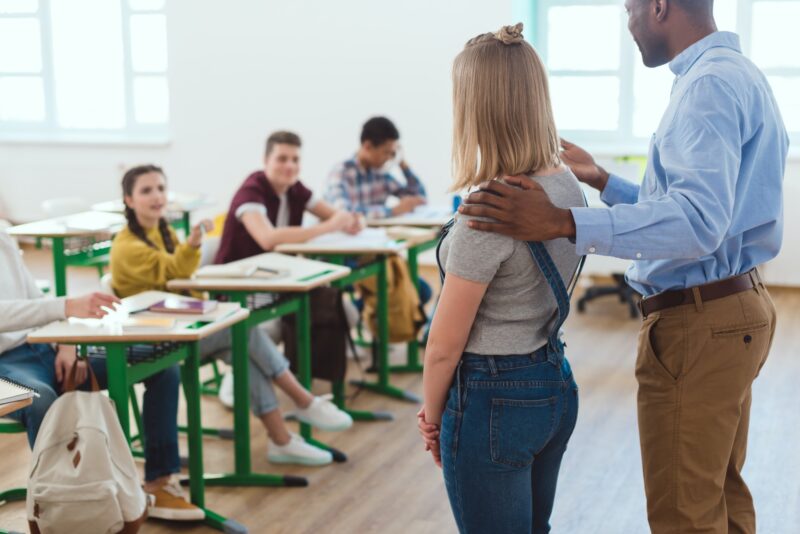 African american teacher introducing new girl to multicultural classmates