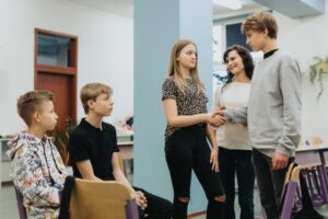 Two friends at odds shake hands during a workshop with a psychologist at school