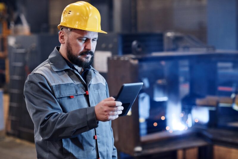 Male engineer or builder in workwear using tablet for checking data about goods
