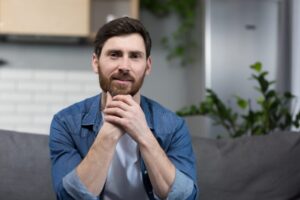 Portrait of a man with a beard at home, sitting on the couch and looking at the camera