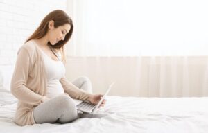 Pregnant woman working on laptop at home during maternity leave