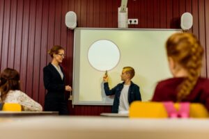 teacher and schoolkids looking at boy making presentation at interactive whiteboard