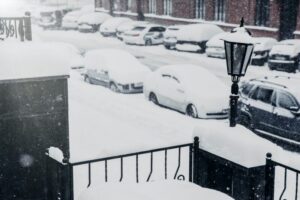Cars covered with snow stand in parking lot, being paralysed because of bad weather conditions