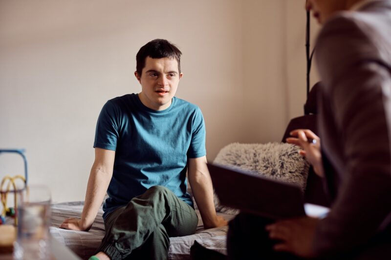 Young man with down syndrome talking to special education tutor during home visit.