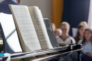 School choir, piano with notes on foreground and students defocused at the background