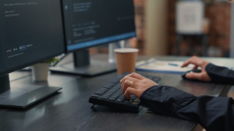 Closeup of developer hands typing code on keyboard while looking at computer screens