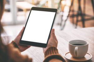 A woman holding black tablet pc with blank white screen with coffee cup on wooden table
