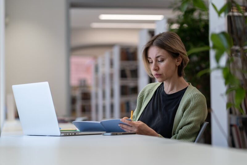 Concentrated female university professor checking course schedule while sitting in empty library