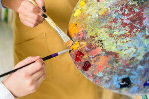 cropped image of teacher and pupil taking same paint from palette in workshop of art school