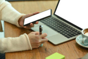Cropped shot young woman holding mobile phone and making notes on sticky note.