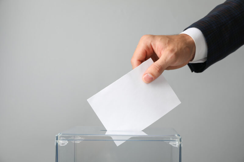 Man putting ballot into voting box on gray background