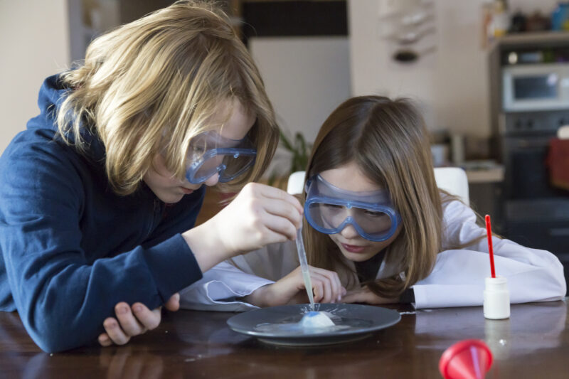 Two children wearing safety glasses using chemistry set at home