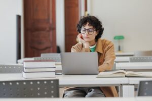 thoughtful woman in library, watches online training webinar and takes notes in notebook.