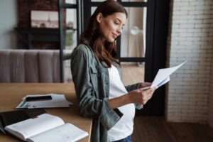 Happy pregnant woman working with papers and laptop