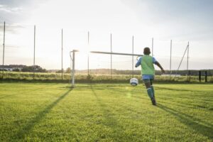 Young football player on football ground at sunset