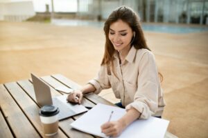 Glad millennial mixed race lady brunette student in headphones sitting at table with laptop