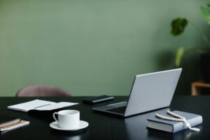 Office workplace desk with open laptop against green wall