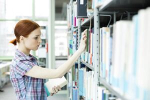 Student in a university library taking book from shelf