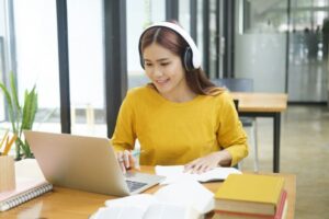 Woman learning online using laptop and writing notes.