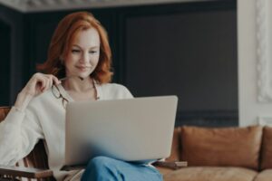 Horizontal shot of happy skilled ginger woman teacher works distantly