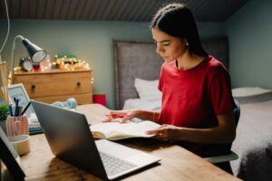 Young hispanic woman writing down notes while working with laptop