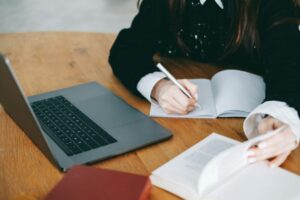 Young woman college student taking notes, studying with laptop in library.