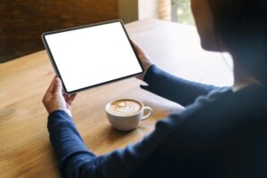 A woman holding black tablet pc with blank white screen with coffee cup on wooden table