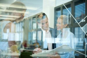 Smiling business team behind glass wall in office looking at folder