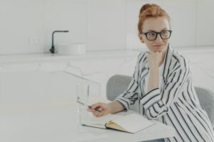 Thoughtful redhead woman distracted from work makes notes in notepad holds pen