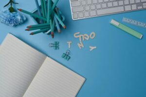 Empty notebook, keyboard and pencil holder on blue background.