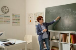 Young teacher of physics explaining formulas on blackboard
