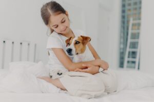 Photo of relaxed beautiful small girl plays with pedigree dog, embraces favourite animal