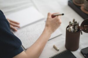Close up and selective pens and pencils in brown pencil box with blurred hand writing on notebook.