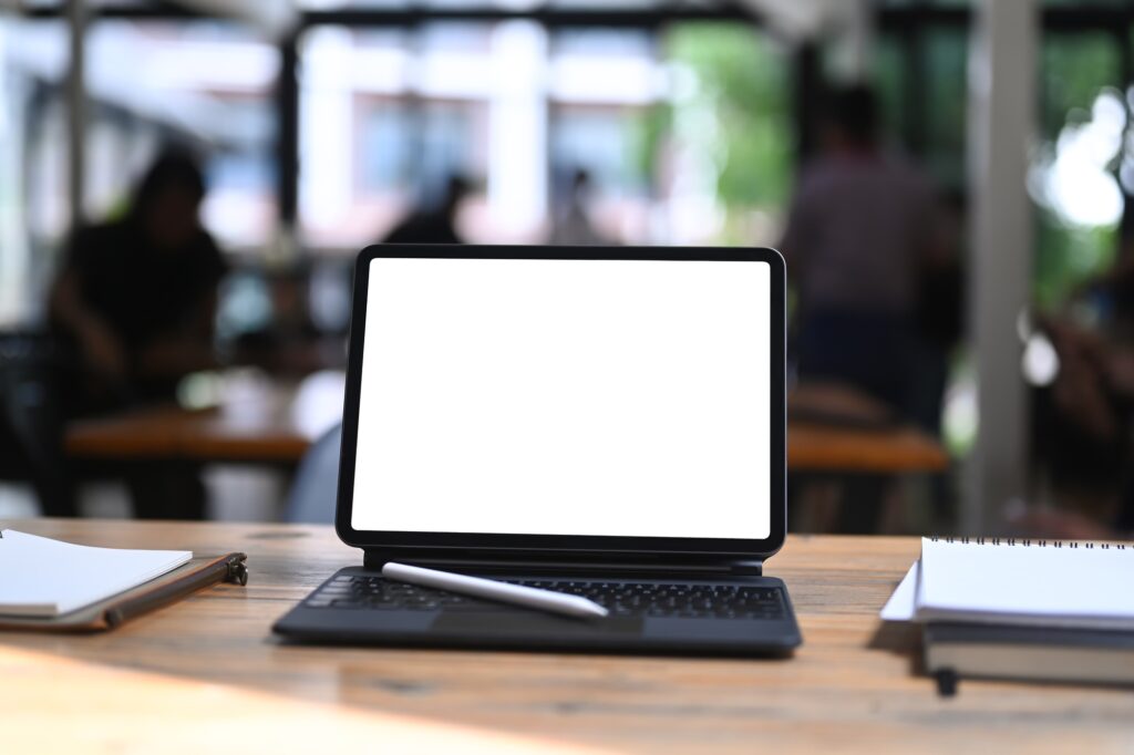 Computer tablet with empty screen, stylus pen and books on wooden table.