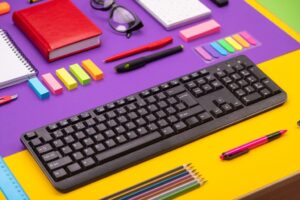 Modern working place with keyboard, diary, pencils, pens and glasses on orange-purple background