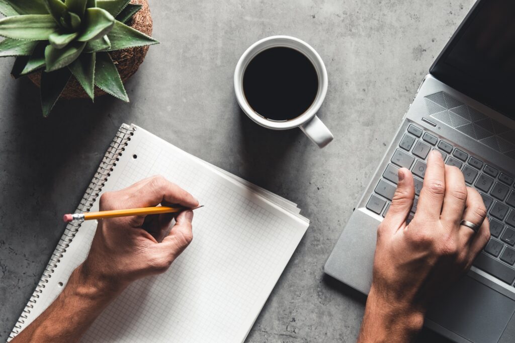 The office desk flat lay view with laptop, mouse, tree, paper clip, coffee cup, notebook, pencil