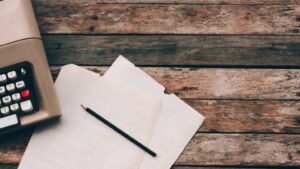 Typewriter, pensil and paper on wooden background.