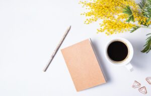 Flat lay with yellow mimosa flower, cup of coffee, craft notebook and pencil on a marble table