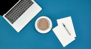 Top view of a cup of coffee, laptop, papers, and a pen on a blue surface
